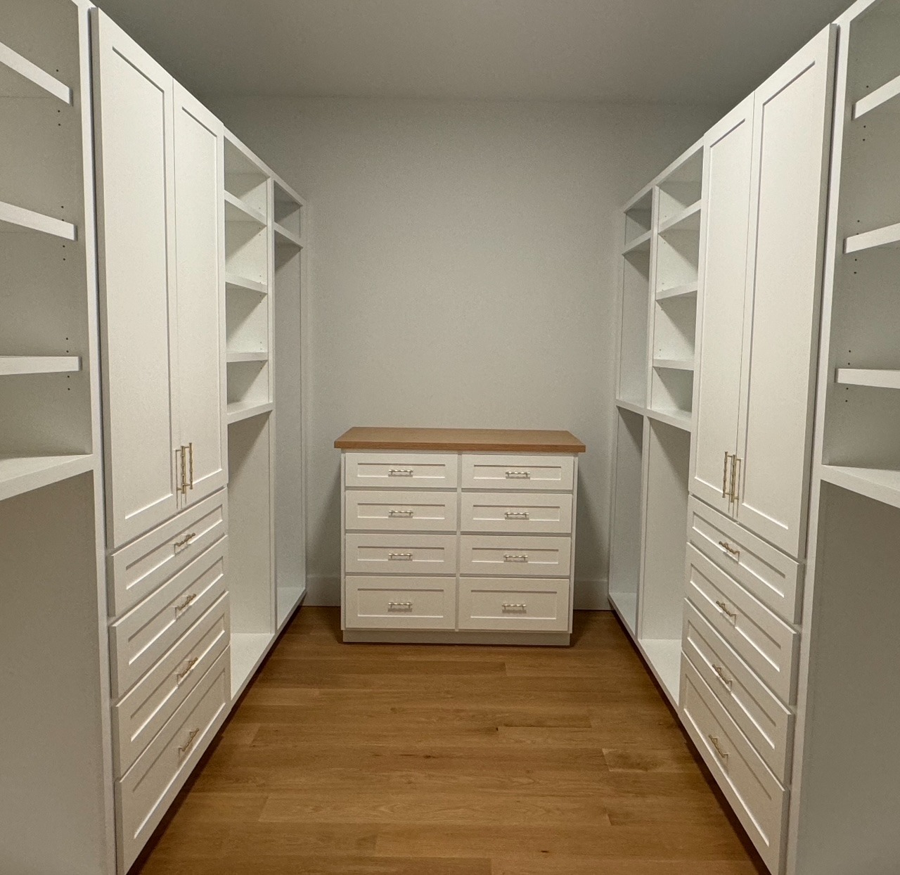 Custom walk-in primary closet with painted cabinetry, drawers, open shelving, and natural wood tops