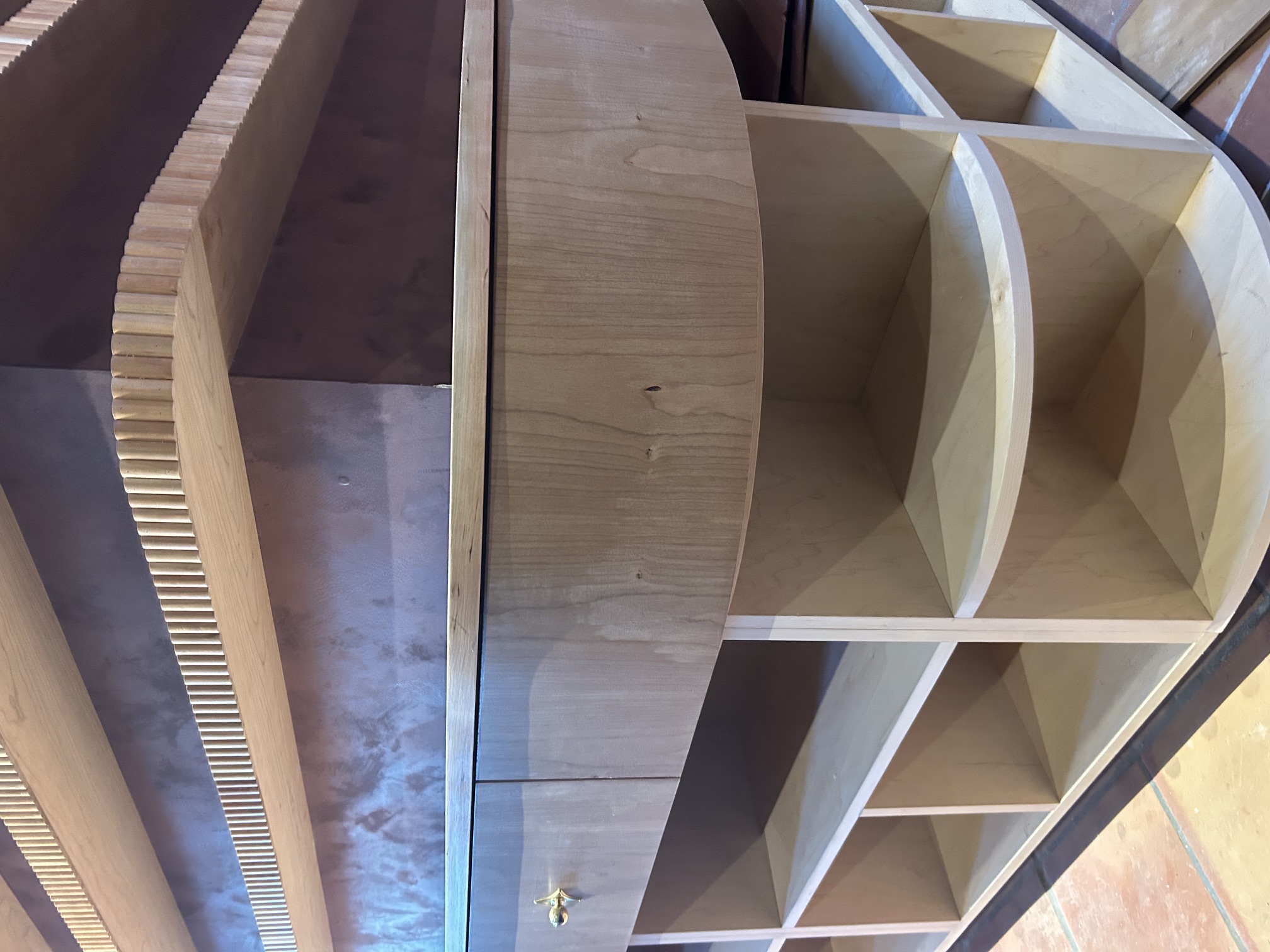 Close detail of curved cherry display cabinetry with open storage below